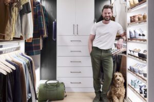 Walk-in cloffice designed for Netflx’s Bobby Berk allows for work items plus clothing samples in white wood finish created by California Closets