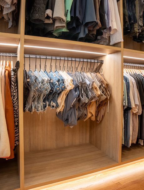 Walk in closet designed to hang everything up with hook hangers for denim and LED lighting to easily find items by California Closets