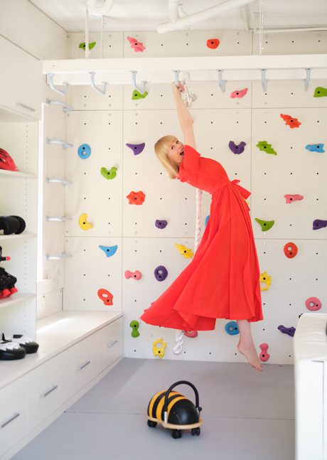 Erin Fetherston hanging from a jungle gym in the playroom she converted from a garage. The design incorporated extra storage with built in cabinets and open shelving by California Closets.
