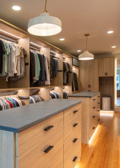Long walkway walk in closet design with center islands led lighting and custom cabinets in natural wood finish by California Closets