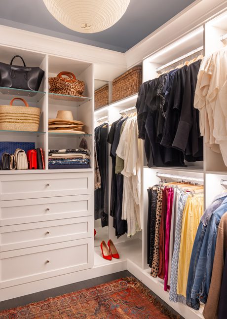 Custom glass shelves, slat drawers, hanging racks and LED lights in a walk in closet designed by California Closets