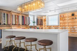 Commercial showroom design with open shelving, hanging poles, LED lighting, custom drawers and storage in natural and linen finishes by California Closets