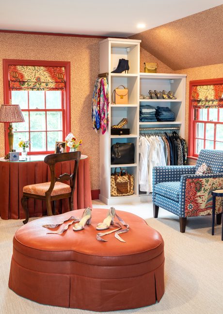 Large walk in closet, dressing room and sitting area designed in a converted attic with shoe shelving, wardrobe organizers and a center ottoman, designed by California Closets
