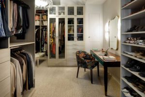 Walk in closet designed with floor to ceiling storage, shoe racks and a custom vanity space with light wood grain finish by California Closets