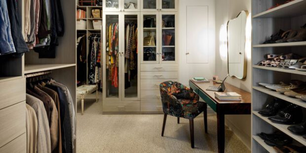 Walk in closet designed with floor to ceiling storage, shoe racks and a custom vanity space with light wood grain finish by California Closets