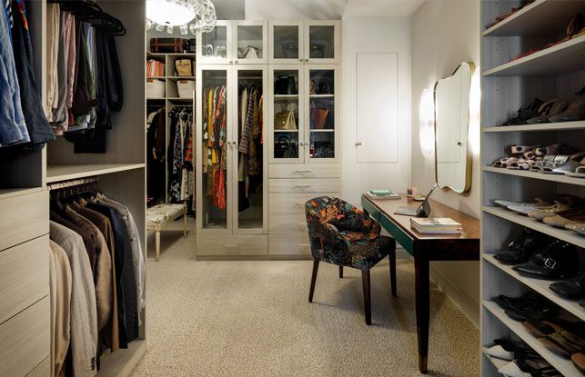 Walk in closet designed with floor to ceiling storage, shoe racks and a custom vanity space with light wood grain finish by California Closets