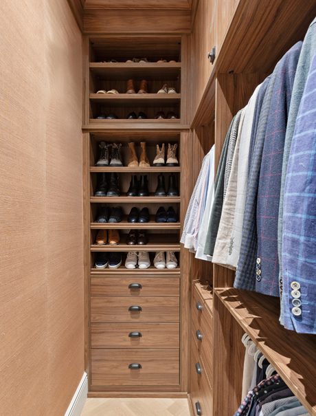 His walk in closet design with shoe racks, custom drawers and open hanging poles by California Closets