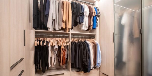 Glass door closet design with wood grain finish and LED lighting created by California Closets