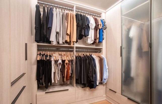 Glass door closet design with wood grain finish and LED lighting created by California Closets