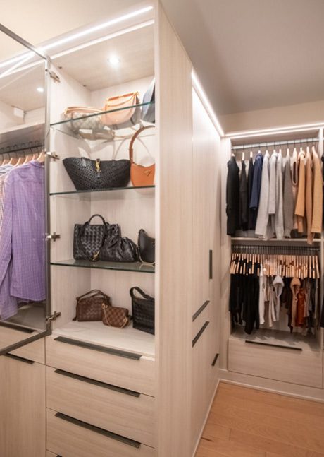 Glass shelving in a walk in closet to store purses with LED lighting created by California Closets